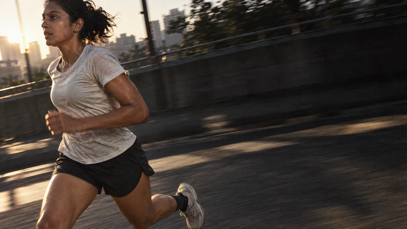 A woman runs along a raised city road at first light, the traffic blurred behind her.